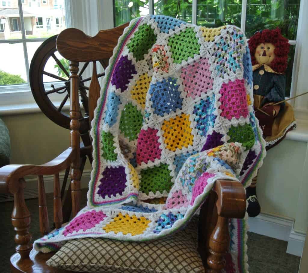 the Granny Square Scrap-ghan on a rocking chair in front of a window