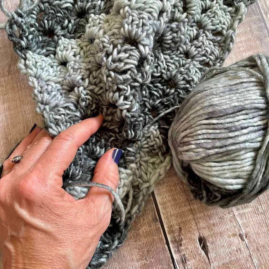 Picture of a hand touching the scarf with a ball of yarn