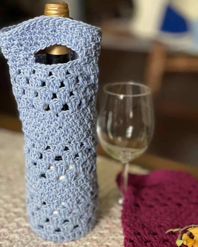 Picture of a wine bottle in a wine bottle tote with a wine glass | The Seneca Wine Bottle Tote is a crochet design by MadameStitch