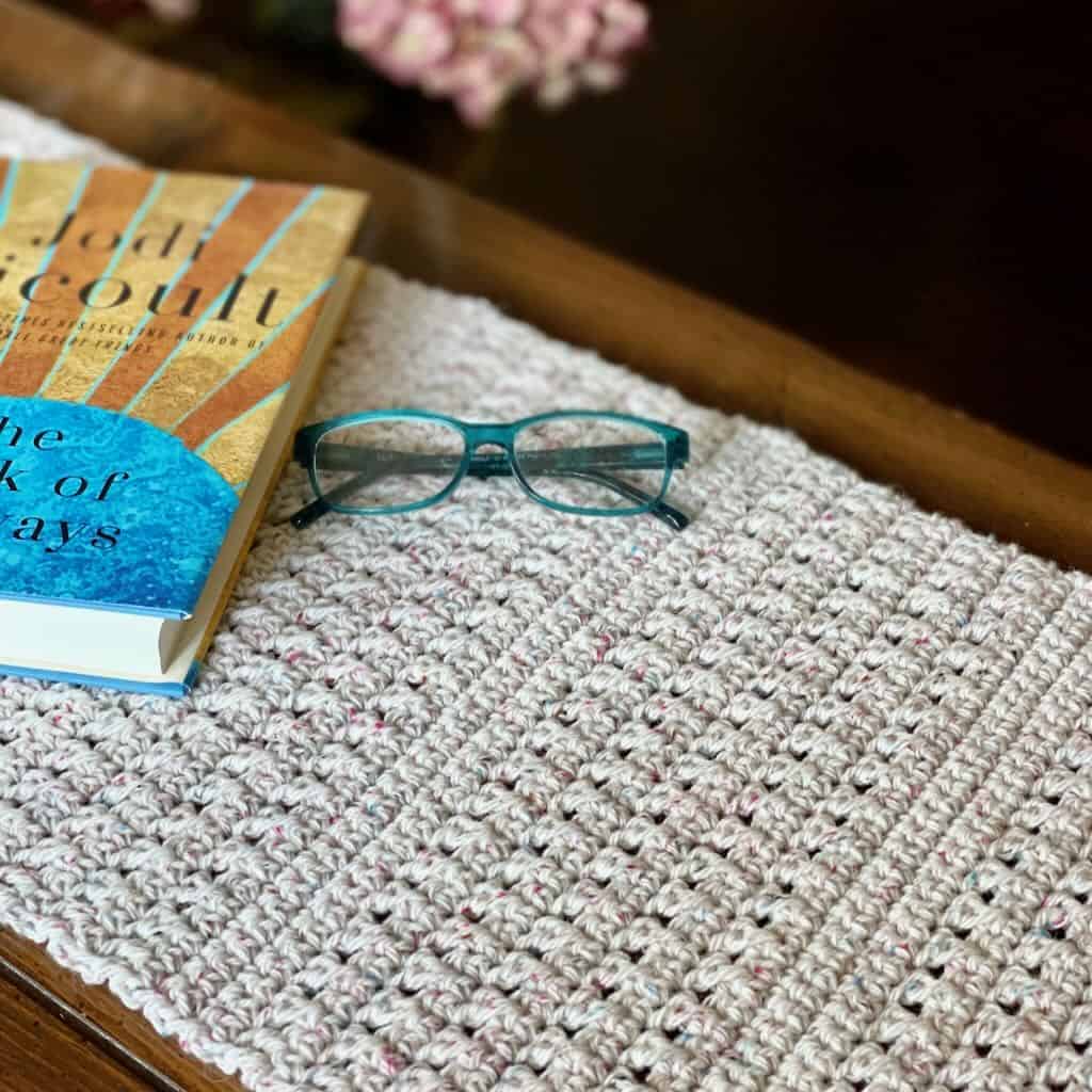 A crochet table runner with a book and glasses | The Pathways Table Runner crochet pattern is free on the blog