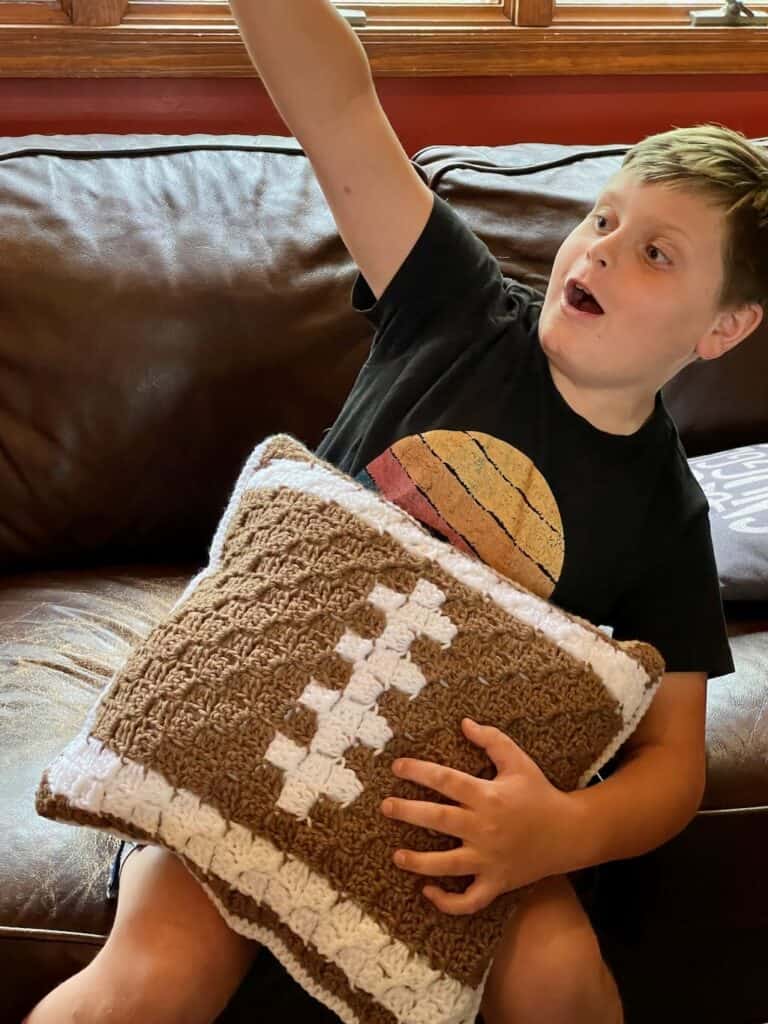 A photo of a boy cheering for the football game, holding his football pillow