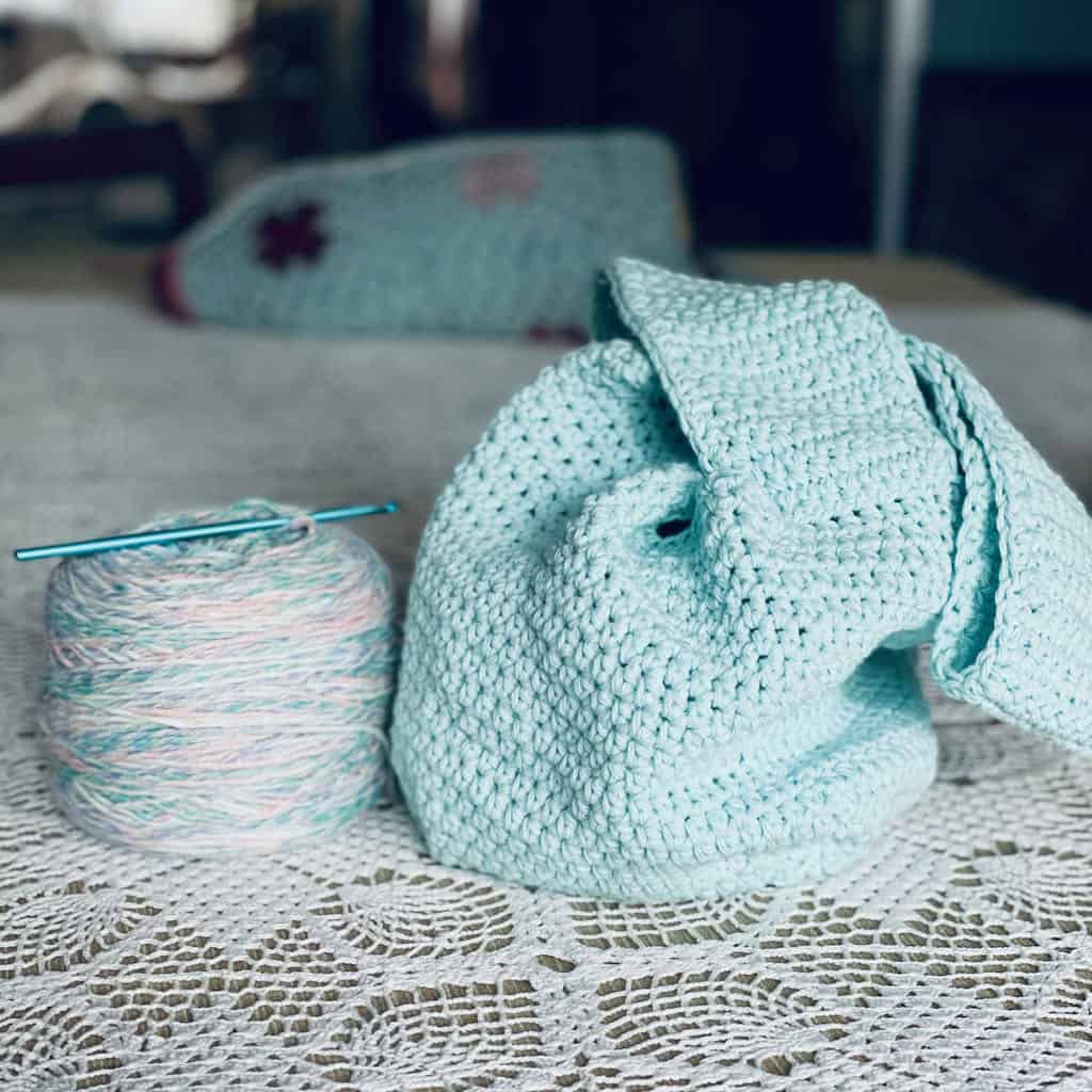 A photo of the ami project bag sitting on a crochet table cloth next to a ball of yarn