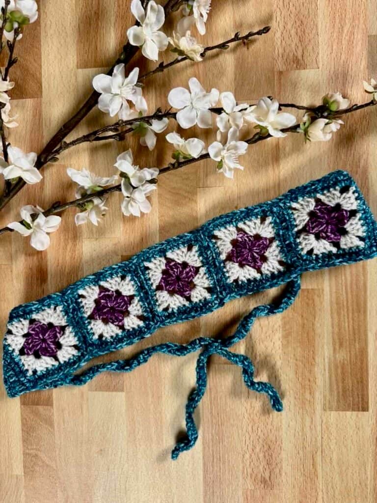 Crochet granny square headband in three colors laid flat on a wooden surface