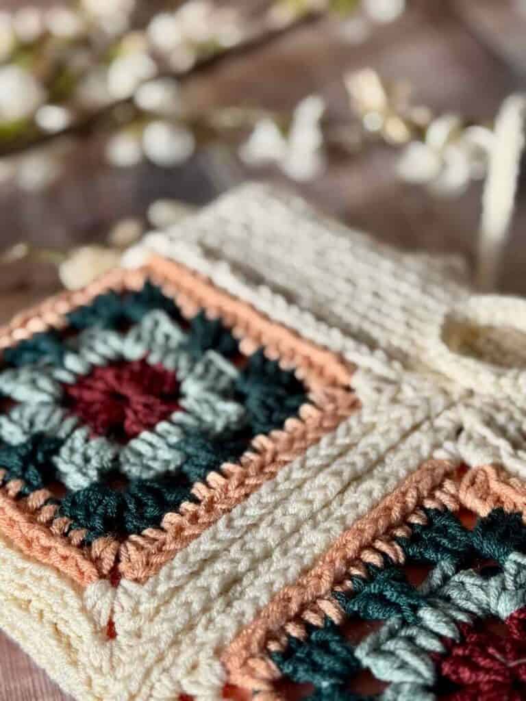 A photo of the granny square book sleeve on a wooden background with flowers