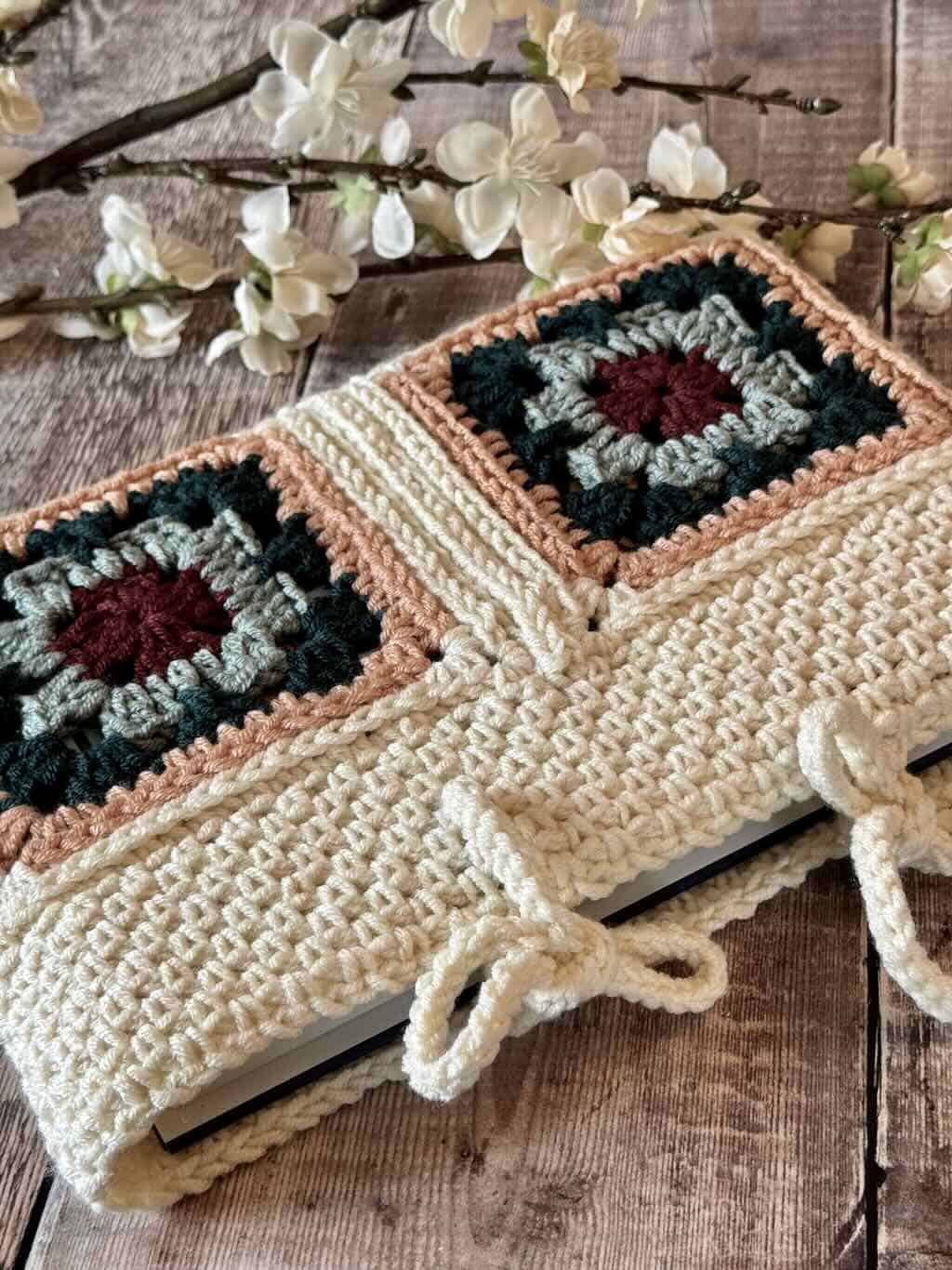 A closeup of the granny square book sleeve on a wooden background with flowers