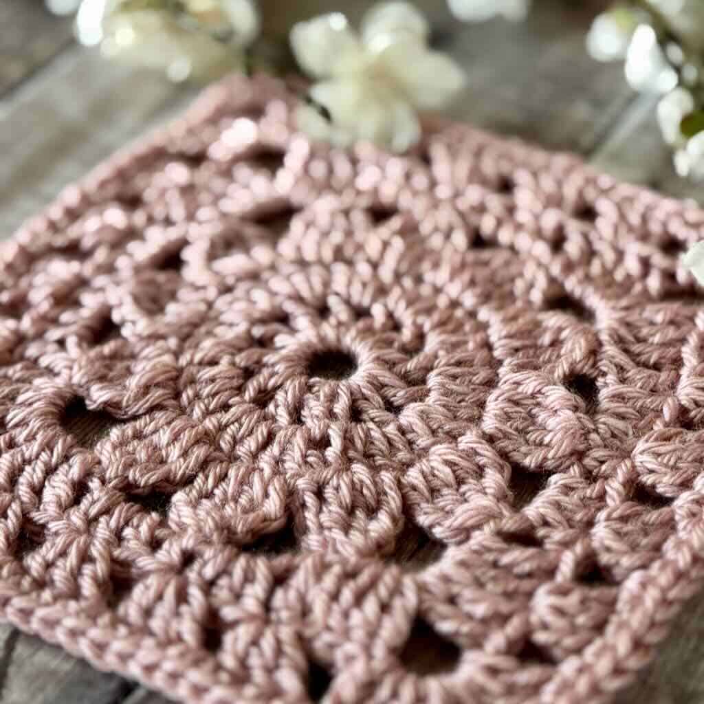 A closeup of the Compass Rose granny square with flowers in the background