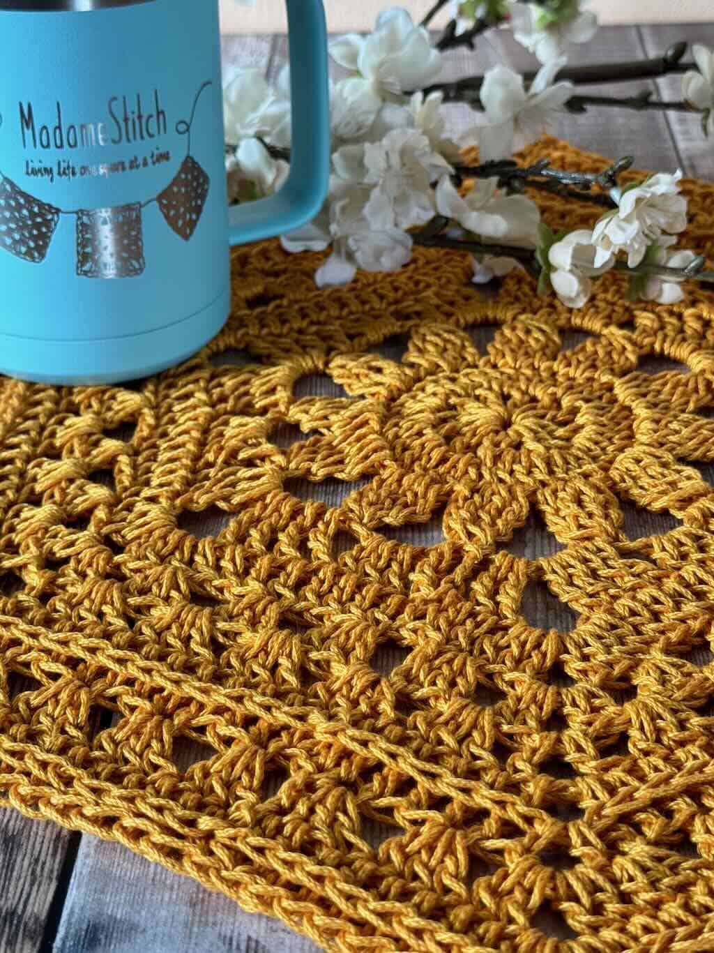 A photo of the crochet hexagon placemat with flowers with a cup