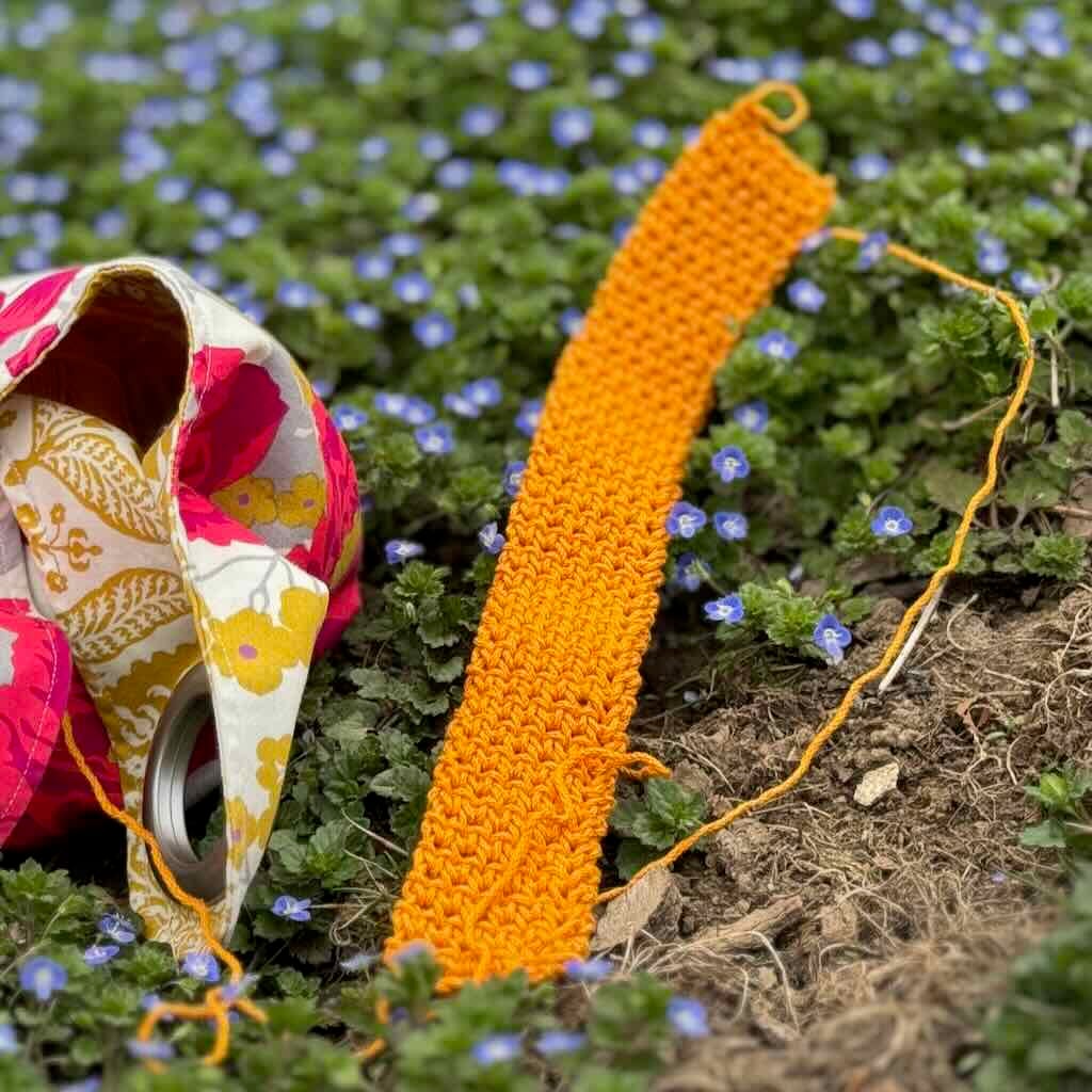 A photo of a single crochet thermal stitch strap lying in a bed of flowers