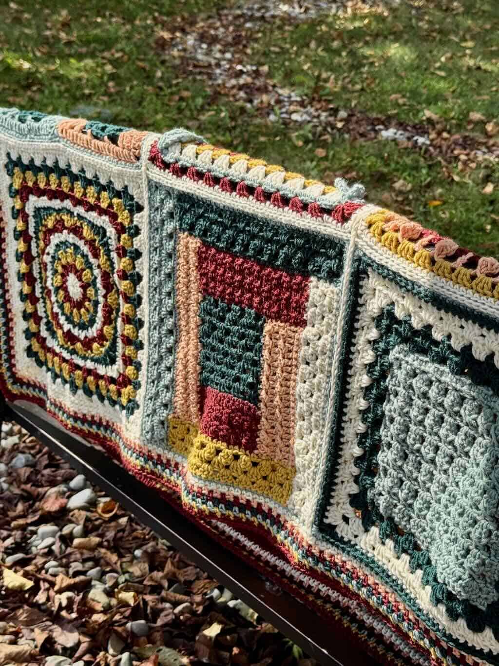 A photo of the Granny Stitch Sampler Blanket hanging on a bench
